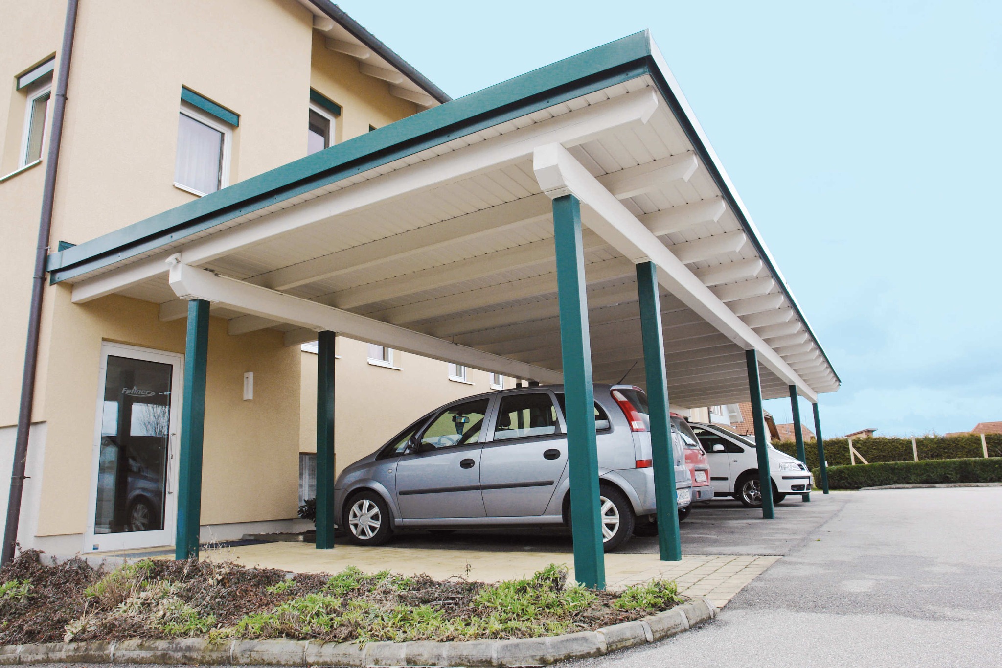 Großzügiger Carport mit weißer Holzkonstruktion und grün lackierten Holzstützen
